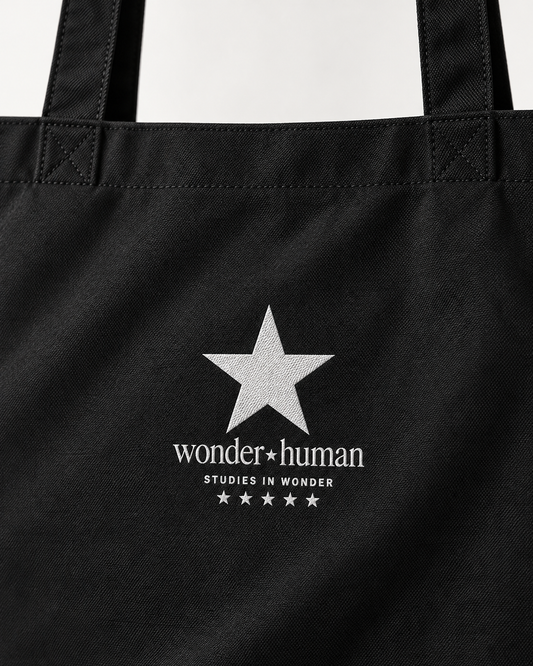 Close-up of black North Star Tote Bag showing white star, Wonder Human logo, and cotton fabric texture