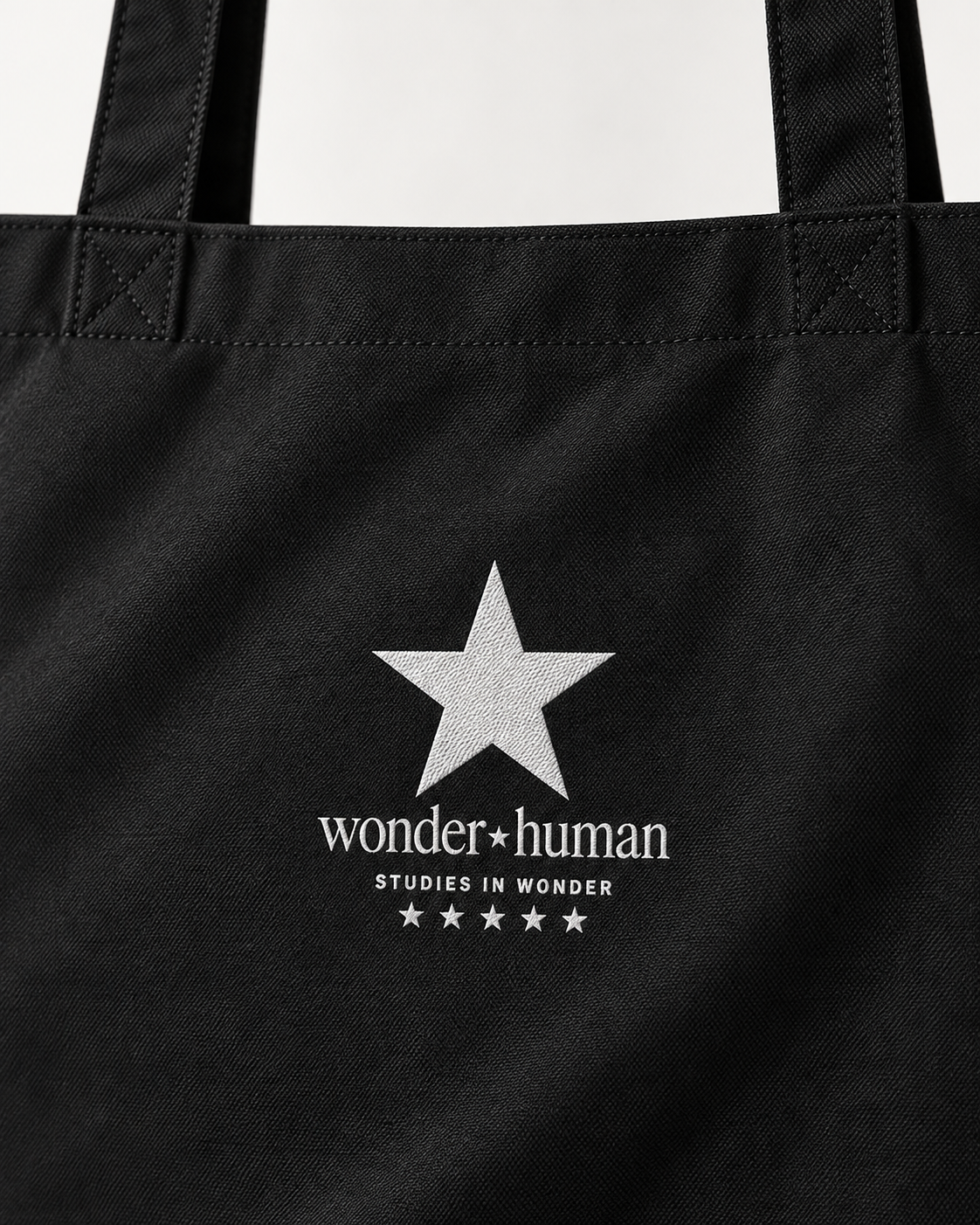 Close-up of black North Star Tote Bag showing white star, Wonder Human logo, and cotton fabric texture
