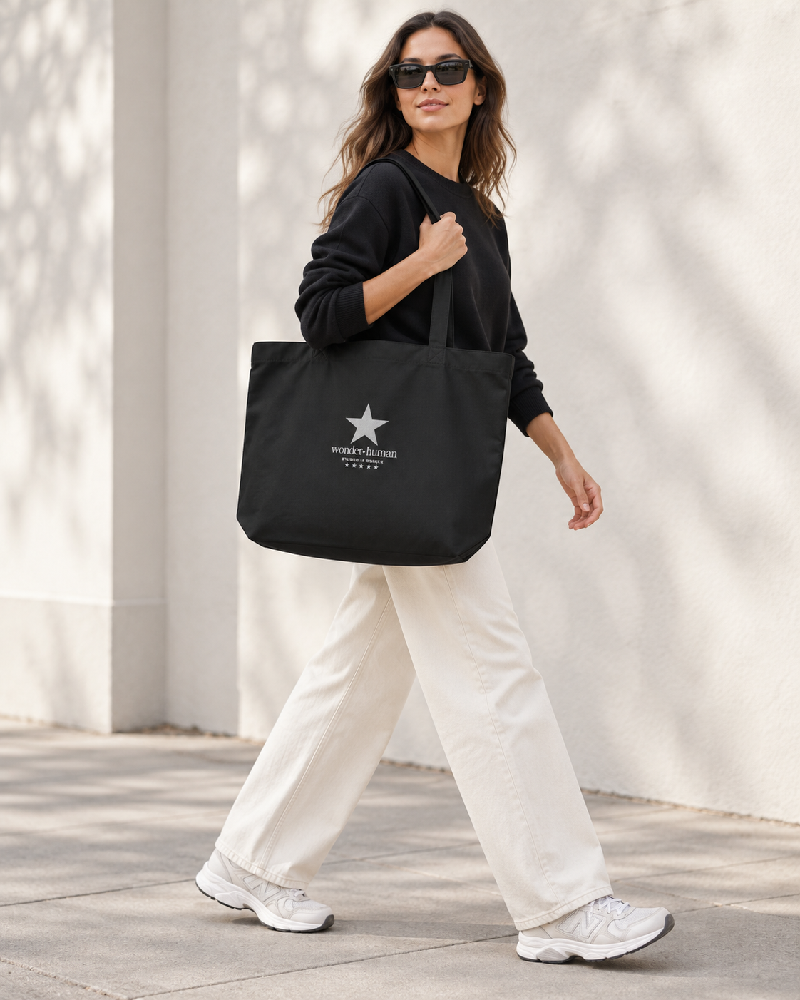 Woman walking with black North Star Tote Bag styled with black sweatshirt and cream pants